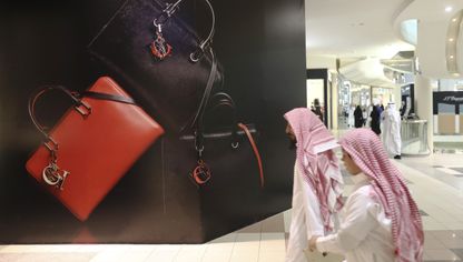 متسوقان بالزي الوطني السعودي يمران أمام إعلان للحقائب الفاخرة في أحد المراكز التجارية في الرياض - بلومبرغ