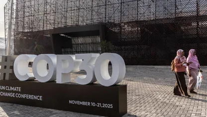 سيدتان تمران بجوار لافتة تحمل شعار "كوب 30" خارج متنزه "باركي دا سيدادي"، المقر الرئيسي لانعقاد القمة في مدينة بيليم بولاية بارا البرازيلية - بلومبرغ