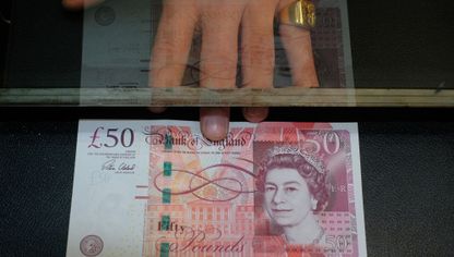 شخص يمسك بعملة نقدية فئة 50 جنيهاً إسترلينياً - المصدر: بلومبرغ