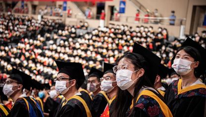 طلاب صينيون من جامعة "هواتشونغ" للعلوم والتقنية يتابعون فيلماً قصيراً على شاشة عرض ضخمة خلال احتفال التخرج بصالة للألعاب الرياضية بالكلية - المصدر: بلومبرغ