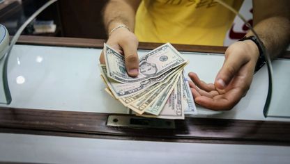شخص يمسك أوراقاً نقدية من الدولار الأميركي - المصدر: بلومبرغ