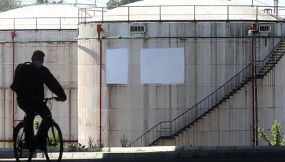 رجل يقود دراجته الهوائية بالقرب من خزانات نفط في منشأة تديرها شركة "غازبروم نفط" في العاصمة الصربية بلغراد - المصدر: بلومبرغ