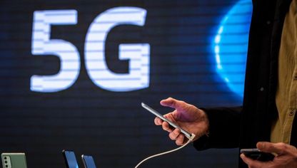 شخص يحمل هاتفاً ذكياً وفي الخلفية شعار 5G.. شبكة الجيل الخامس للاتصالات تتيح سعات وتحميلاً أكبر للمشتركين وتخلق جيلاً جديداً من التطبيقات التكنولوجية - المصدر: بلومبرغ