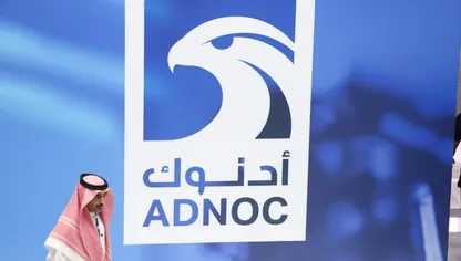 شخص يمر أمام لوحة إعلانية تحمل شعار "أدنوك" الإماراتية - بلومبرغ