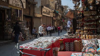 أشخاص يمرون أمام بضائع معروضة بأحد الشوارع في مصر - المصدر: بلومبرغ