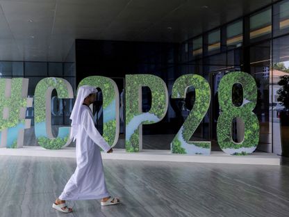 أحد الأشخاص يمر أمام لافتة خاصة بقمة المناخ \"كوب 28\" الإمارات (COP28) وُضعت خلال ورشة عمل للقيادة الفكرية على مستوى المسؤولين التنفيذيين للتركيز على العمل المناخي، في العاصمة الإماراتية أبوظبي، يوم 1 أكتوبر 2023 - المصدر: رويترز