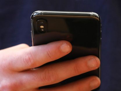 عميل يرتدي قميصاً يحمل شعار \"أبل\" يختبر هاتف \"iPhone X\" بمتجر في لندن - المصدر: بلومبرغ