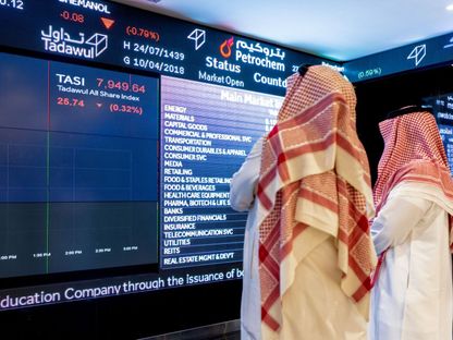 شخصان يطالعان بيانات أسعار الأسهم على لوحة معلومات إلكترونية في سوق الأسهم السعودية 'تداول'. صورة أرشيفية - المصدر: بلومبرغ