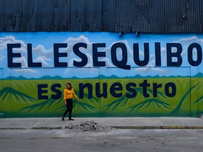 إمرأة تمر أمام لوحة جدارية كُتب عليها \"إيسيكويبو لنا\" في إشارة إلى المنطقة المتنازع عليها، وذلك يوم التصويت على الاستفتاء في العاصمة الفنزويلية كاراكاس، الأحد في 3 ديسمبر 2023 - المصدر: بلومبرغ