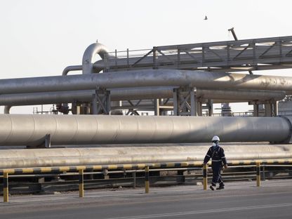 عامل يسير قرب أنابيب لنقل النفط في محطة لمعالجة الخام تابعة لـ\"أرامكو السعودية\" في بقيق، المملكة العربية السعودية - المصدر: بلومبرغ