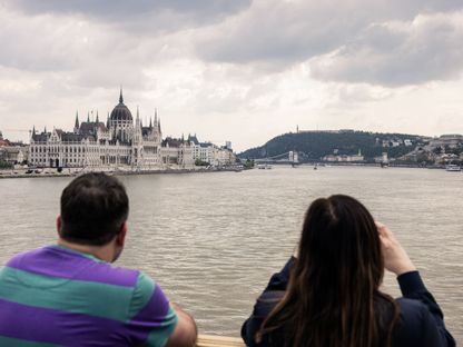 سائحان يلقيان نظرة على البرلمان المجري على الضفة المقابلة من نهر الدانوب، في بودابست، المجر - المصدر: بلومبرغ