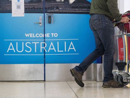 راكب يمر قرب باب كتب عليها استراليا ترحب بك في مطار سيدني - المصدر: بلومبرغ