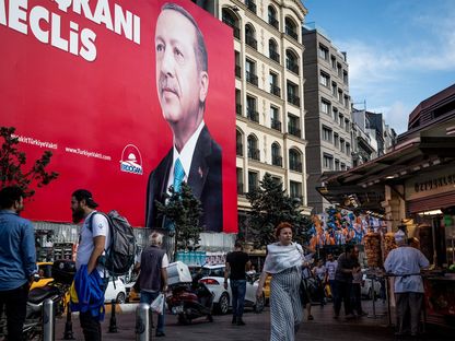 أشخاص يمرون أمام ملصق انتخابي يظهر صورة الرئيس التركي رجب طيب أردوغان في إسطنبول. - المصدر: بلومبرغ