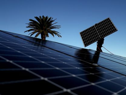 عامل يحمل لوحاً كهروضوئي لاستجرار الطاقة الشمسية لتركيبه على سقف في أستراليا - المصدر: بلومبرغ