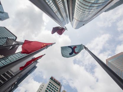 علم بورصة هونغ كونغ (يميناً) والعلم الصيني (يساراً) وهو يرفرف خارج مجمع إكستشينج سكوير في هونغ كونغ، الصين - المصدر: بلومبرغ