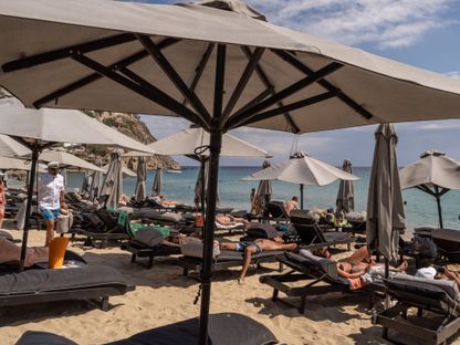 سياح يستلقون على كراسٍ تحت المظلات على شاطئ إليا، ميكونوس، اليونان، خلال شهر يونيو الماضي - المصدر: بلومبرغ