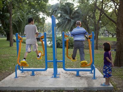فتاة صغيرة، على اليمين، تشاهد رجلاً مسناً، في الوسط، يمارس التمارين الرياضية في حديقة لومفيني في بانكوك، في 15 مارس 2015 - المصدر: بلومبرغ