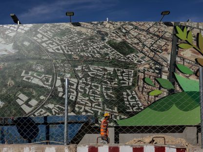عامل بناء يمر أمام لوحية إعلانية لمشروع حديقة الملك سلمان في العاصمة الرياض - المصدر: بلومبرغ