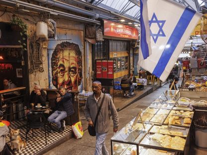 متسوق يمر أمام العلم الإسرائيلي في سوق ماخاني يهودا، القدس - المصدر: بلومبرغ