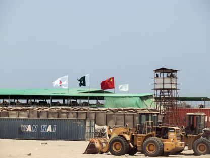 حاوية شحن تابعة لشركة \"وان هاي لاين\" تقف خلف حفارة خارج مخيم للعمال، تديره شركة \" تشاينا أوفرسيز بورتس هولدنغ\"، في جوادار بلوشستان باكستان  - المصدر: بلومبرغ