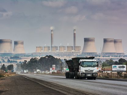شاحنة تعبر على طريق سريع فيما تظهر في الأفق منشأة لتوليد الطاقة تابعة لشركة \"إسكوم\" (Eskom). جنوب أفريقيا - المصدر: بلومبرغ