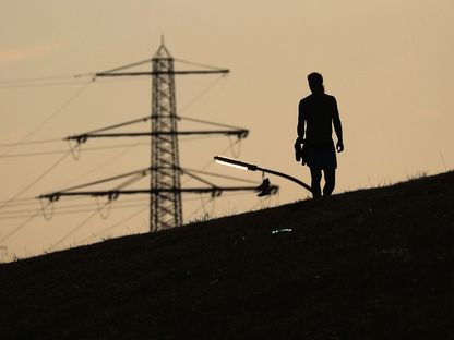 أبراج كهرباء عالية الجهد خلف أحد المشاة على ضفة نهر في هامبورغ، ألمانيا. - المصدر: بلومبرغ