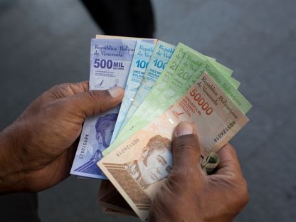 فنزويلي يحمل ورقة جديدة بقيمة نصف مليون بوليفار وأوراق قديمة من فئات 10 آلاف و20 ألف و50 ألف بوليفار خارج أحد البنوك في كاراكاس - المصدر: بلومبرغ