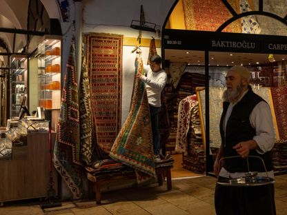 متسوّق يعلّق سجادة خارج متجره في \"البازار الكبير\" في إسطنبول، تركيا.  - المصدر: بلومبرغ