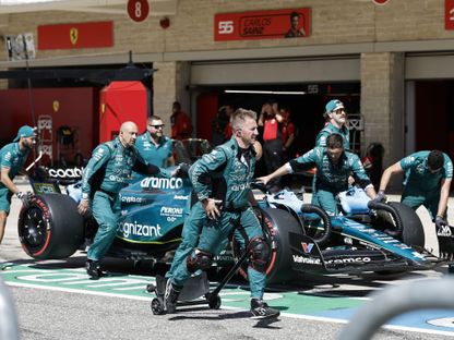 مجموعة من ميكانيكيي \"أستون مارتن\" يدفعون السيارة قبل سباق الجائزة الكبرى للفورمولا 1، الولايات المتحدة - المصدر: بلومبرغ