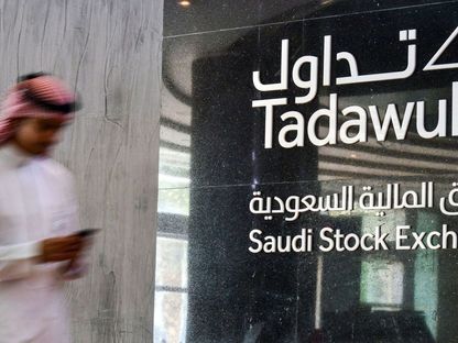 شاب يطالع هاتفه المحمول أمام شعار السوق المالية السعودية 'تداول' في مدخل مقر السوق في الرياض، المملكة العربية السعودية - المصدر: بلومبرغ