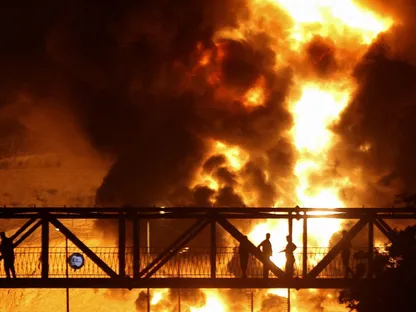 أشخاص يراقبون من جسر ألسنة اللهب تتصاعد من مستودع للنفط إثر هجوم إسرائيلي، في طهران. 15 يونيو 2025 - رويترز