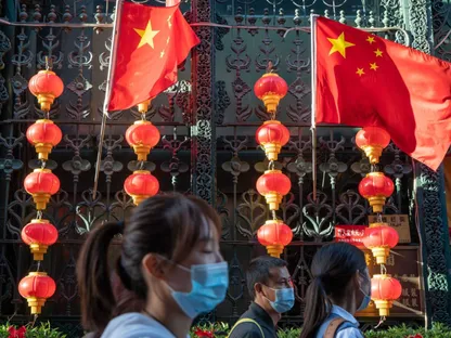 زوار يرتدون أقنعة واقية يسيرون بالقرب من الأعلام الوطنية الصينية والفوانيس الحمراء المزينة للاحتفال بالعيد الوطني في بكين، الصين - المصدر: بلومبرغ