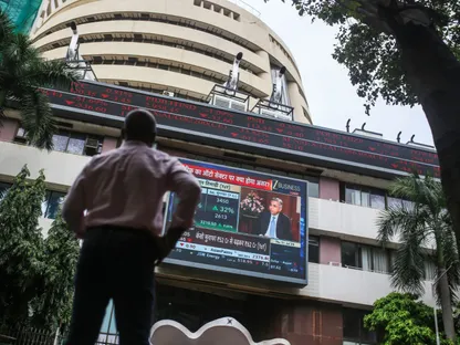 شخص ينظر إلى شاشة تبث برنامجاً عن السوق المالي أمام بورصة \"بومباي\"، في مدينة مومباي بالهند - بلومبرغ