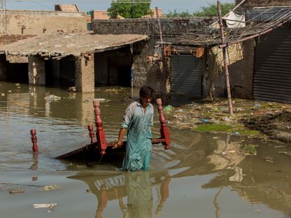 رجل يحاول ينتشل طاولة من مياه الفيضانات بإقليم السند، باكستان - المصدر: بلومبرغ