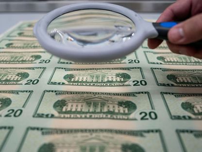 شخص يحمل عدسة مكبرة فوق مجموعة من الأوراق النقدية من فئة 20 دولاراً في واشنطن العاصمة، الولايات المتحدة - المصدر: بلومبرغ