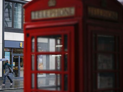 أحد المشاة وراء صندوق هاتف أحمر اللون أثناء مرورها أمام متجر \"إي إي\" للهواتف المحمولة، تديره \"أورانج\" و\"دويتشه تيليكوم\" في لندن، المملكة المتحدة