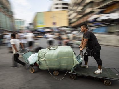 تجار ملابس وحمالون يتنقلون في أنحاء سوق شوخوي للمنسوجات والملابس للجملة في غوانزو في الصين - المصدر: بلومبرغ