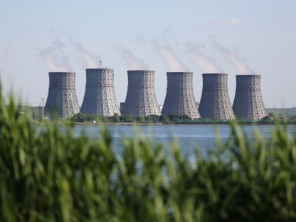 أبراج تبريد متعددة تظهر في الأفق وراء خزان المياه بمحطة الطاقة النووية نوفوفورونز، التي تديرها وحدة \"أو أيه أو روزنرغواتوم\" التابعة لشركة روساتوم في نوفوفورونيغ في روسيا  - المصدر: بلومبرغ