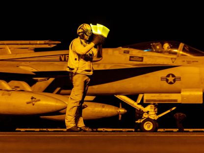 أحد أفراد طاقم مدرج الطيران يشير إلى مقاتلة من طراز \" F/A-18\" سوبر هورنيت أثناء إقلاعها من حاملة الطائرات يو إس إس دوايت دي أيزنهاور جنوب البحر الأحمر، في 19 مارس. - المصدر: بلومبرغ