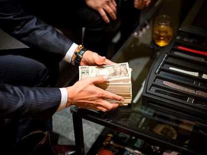 شخص يمسك حزمة من العملة اليابانية فئة 10000 ين في متجر للساعات - المصدر: غيتي إيمجز
