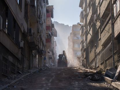 حفار يسير على طول شارع تصطف على جانبيه المباني السكنية المتضررة من الزلازل في هاتاي، تركيا - المصدر: بلومبرغ