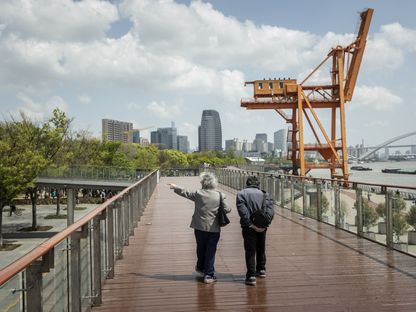 زوجان من كبار السن يسيرا على ممر مرتفع في حديقة بمحاذاة النهر في شنغهاي بالصين - المصدر: بلومبرغ