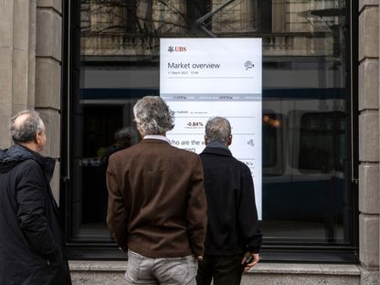 مشاة يتوقفون لمشاهدة لوحة معلومات سوق الأسهم في نافذة المقر الرئيسي لبنك \"يو بي إس غروب\" في زيورخ، سويسرا، يوم الجمعة 17 مارس 2023.  - المصدر: بلومبرغ