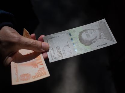 شخص يحمل ورقة نقدية من فئة 200 ألف بوليفار خارج أحد البنوك في العاصمة كاراكاس - المصدر: بلومبرغ