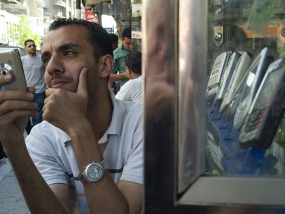 شاب يختبر هاتفاً محمولاً بجانب متجر لبيع أجهزة الاتصالات في القاهرة، مصر - المصدر: بلومبرغ