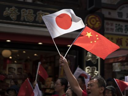 رجل يحمل العلمين الوطنيين الصيني والياباني خلال موكب للاحتفال بالذكرى السبعين لتأسيس جمهورية الصين الشعبية في الحي الصيني في يوكوهاما باليابان في أول أكتوبر 2019.  - المصدر: غيتي إيمجز