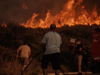 رجال إطفاء ومتطوعون يعملون على إطفاء حقل محترق خلال حريق غابات في سارونيدا، جنوب أثينا، اليونان - المصدر: بلومبرغ