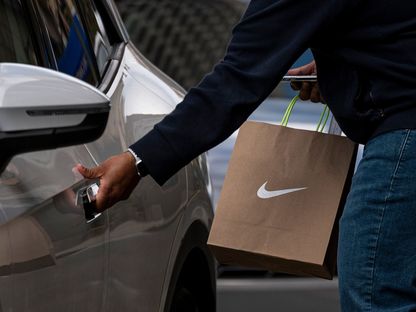 شخص يرتدي قناعاً واقياً يحمل حقيبة تسوق تحمل علامة \"نايكي\" أمام أحد متاجر الشركة في سان فرانسيسكو، كاليفورنيا، الولايات المتحدة - المصدر: بلومبرغ