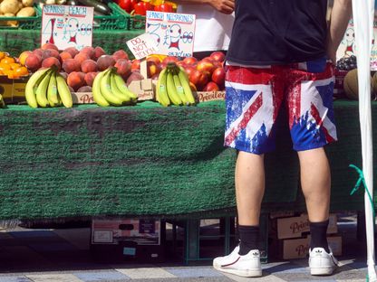 متسوق يرتدي  سروالا قصيرا بنفس لون علم الاتحاد البريطاني ، يشتري الفاكهة من كشك بالسوق في ميدستون ، المملكة المتحدة ، يوم الخميس ، 22 يوليو ، 2021. - المصدر: بلومبرغ