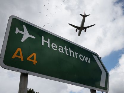 طائرة تحلّق فوق لافتة مرورية تقود إلى مطار هيثرو في لندن، المملكة المتحدة - المصدر: بلومبرغ